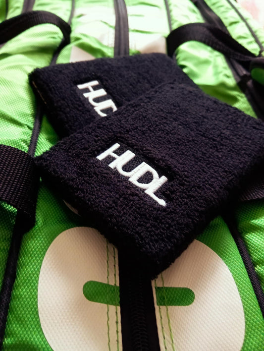 HUDL squash wristbands long two-pack – absorbent sweat bands for squash court performance with the HUDL logo, placed on a green squash bag 